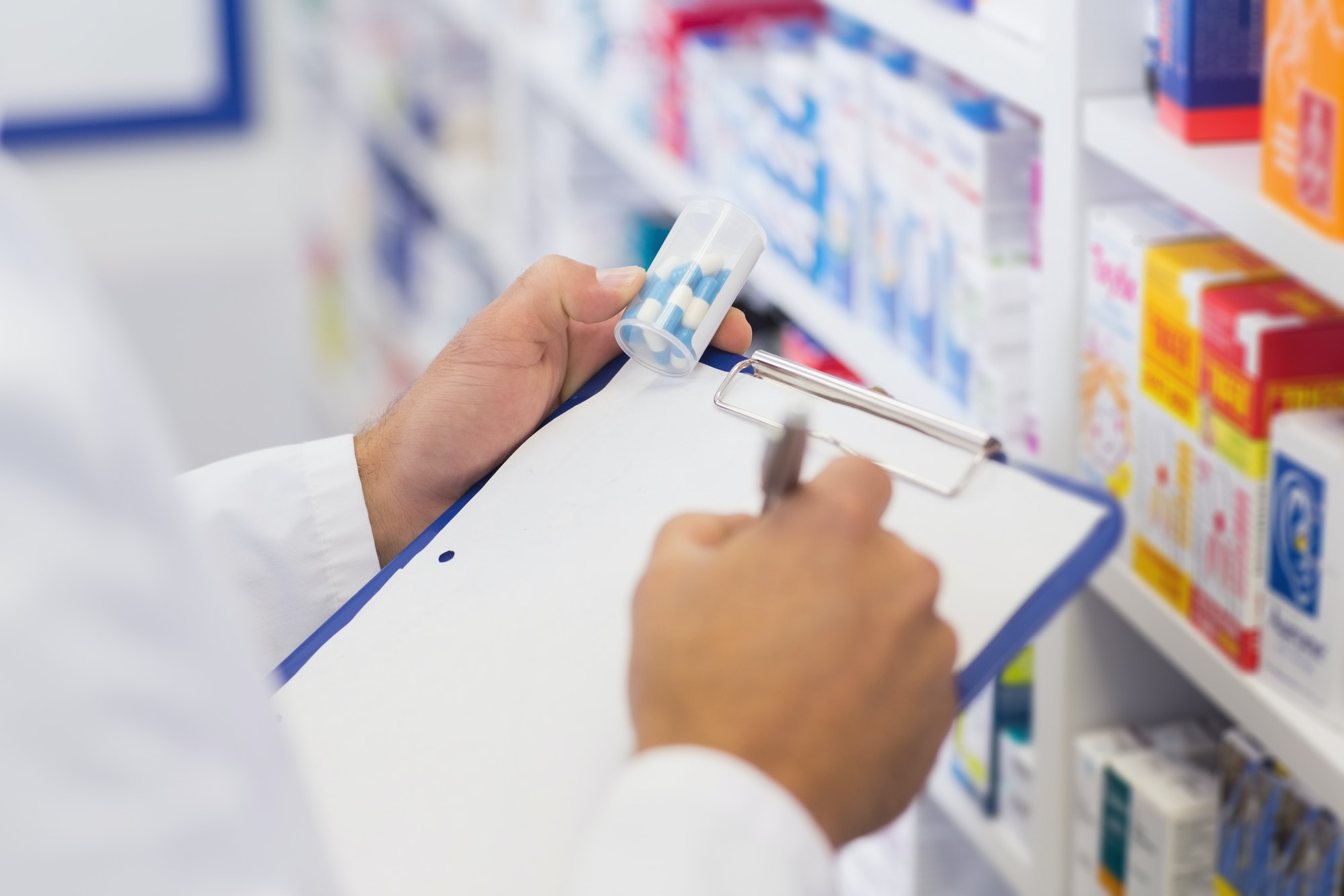 Hospital pharmacist writing on clipboard while holding medication jar