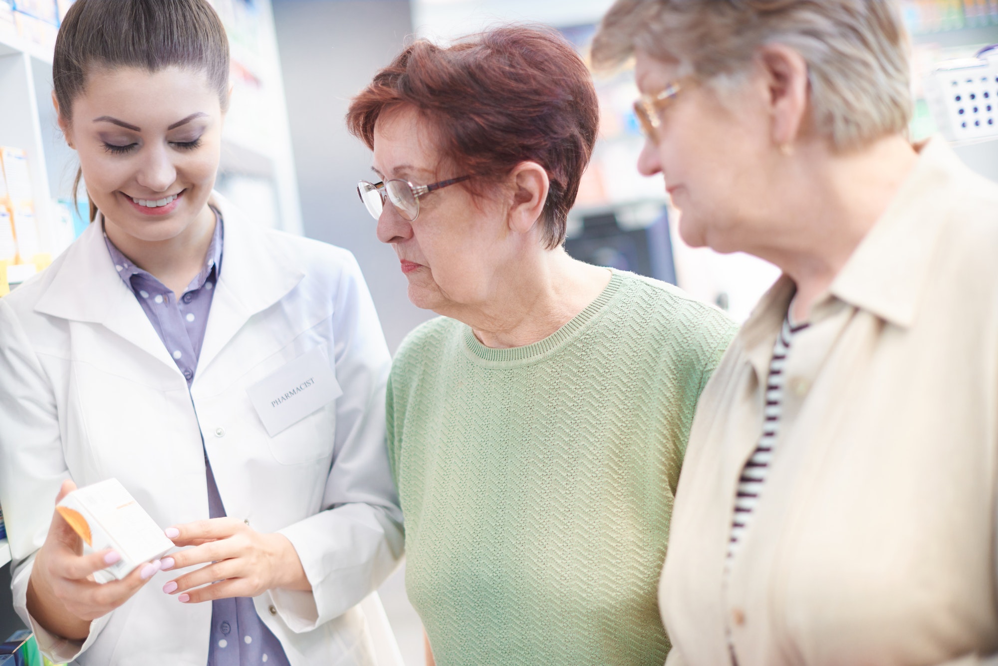 Pharmacist assisting senior clients in drug store aisle